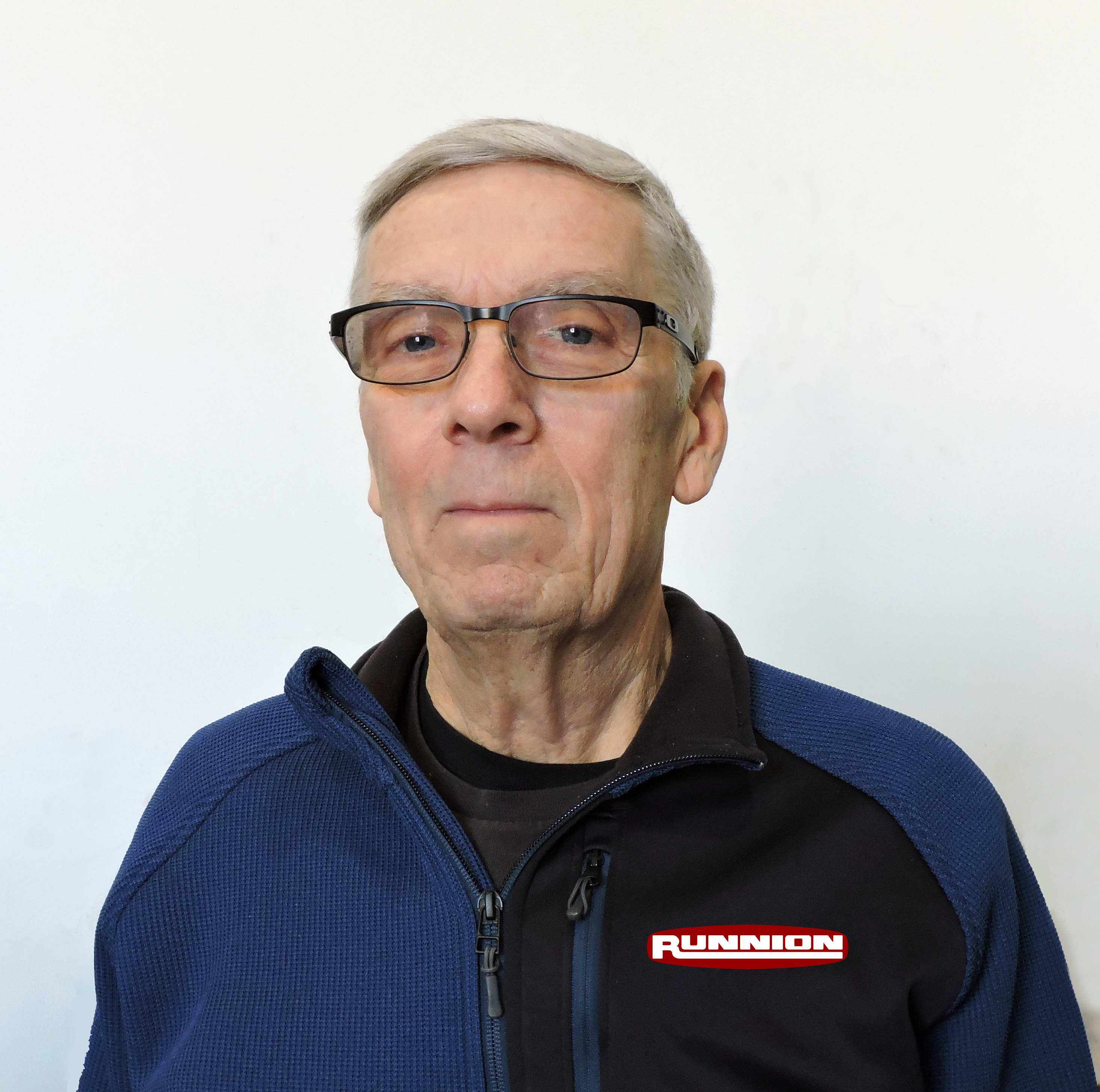 portrait from chest to top of head of a white man with grey hair in a blue zippered fleece sweater