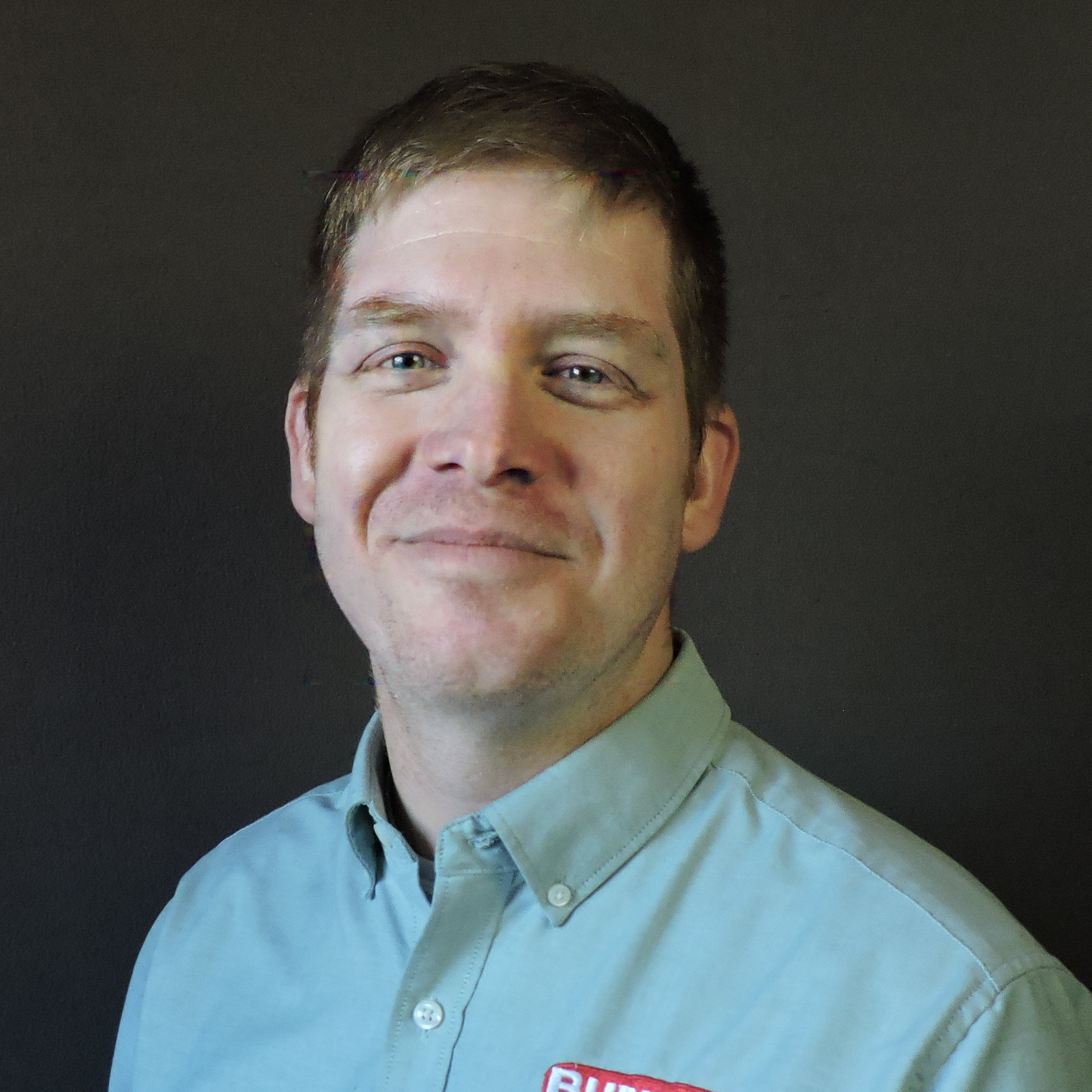 Matt Prochot in a teal shirt smiling in front of a grey background