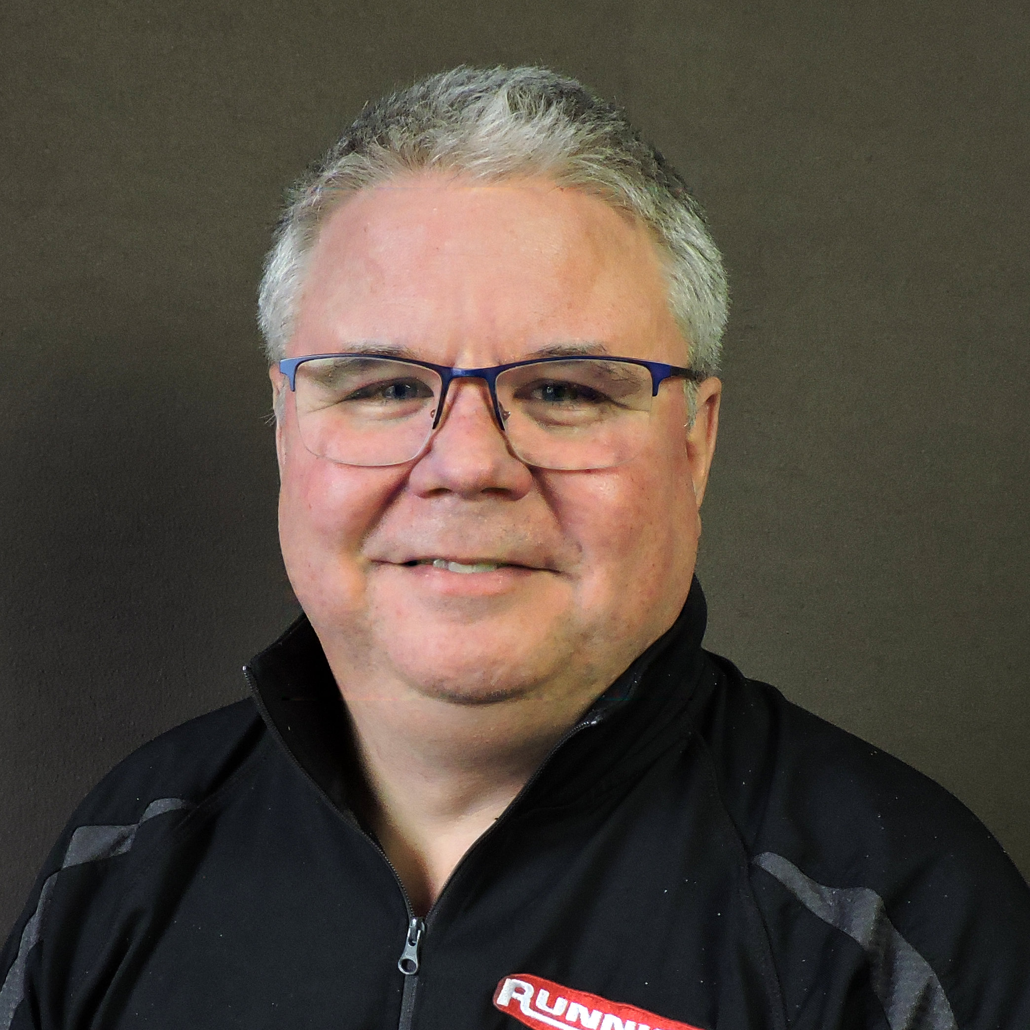 Eric Ingersoll in a black zip up shirt smiling in front of a grey background